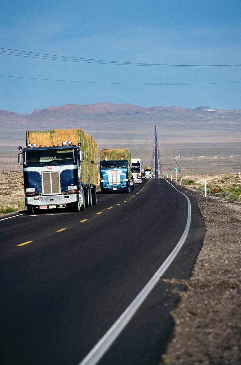 Line of semi-trucks driving on a desert highway near Fallon, Nevada, under a clear blue sky.