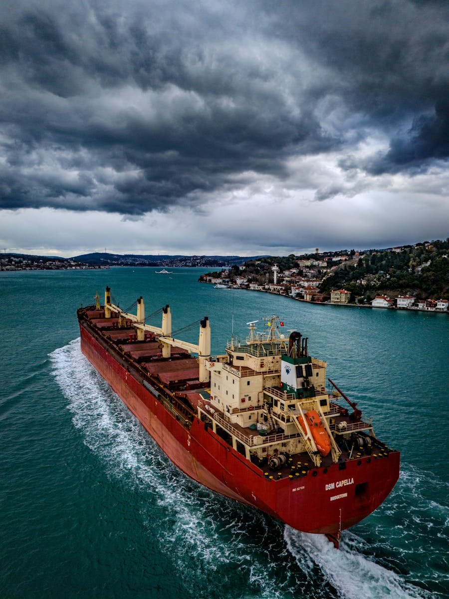 Aerial view of a red cargo ship crossing the Bosphorus Strait under dramatic skies in Istanbul, Turkey.