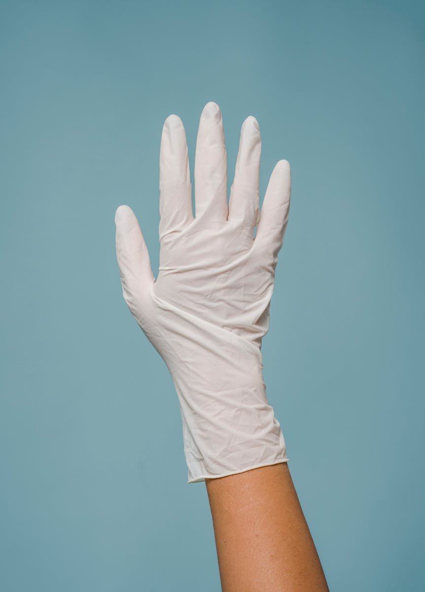 A latex glove-wearing hand raised against a soft blue background, showing hygiene and professionalism.